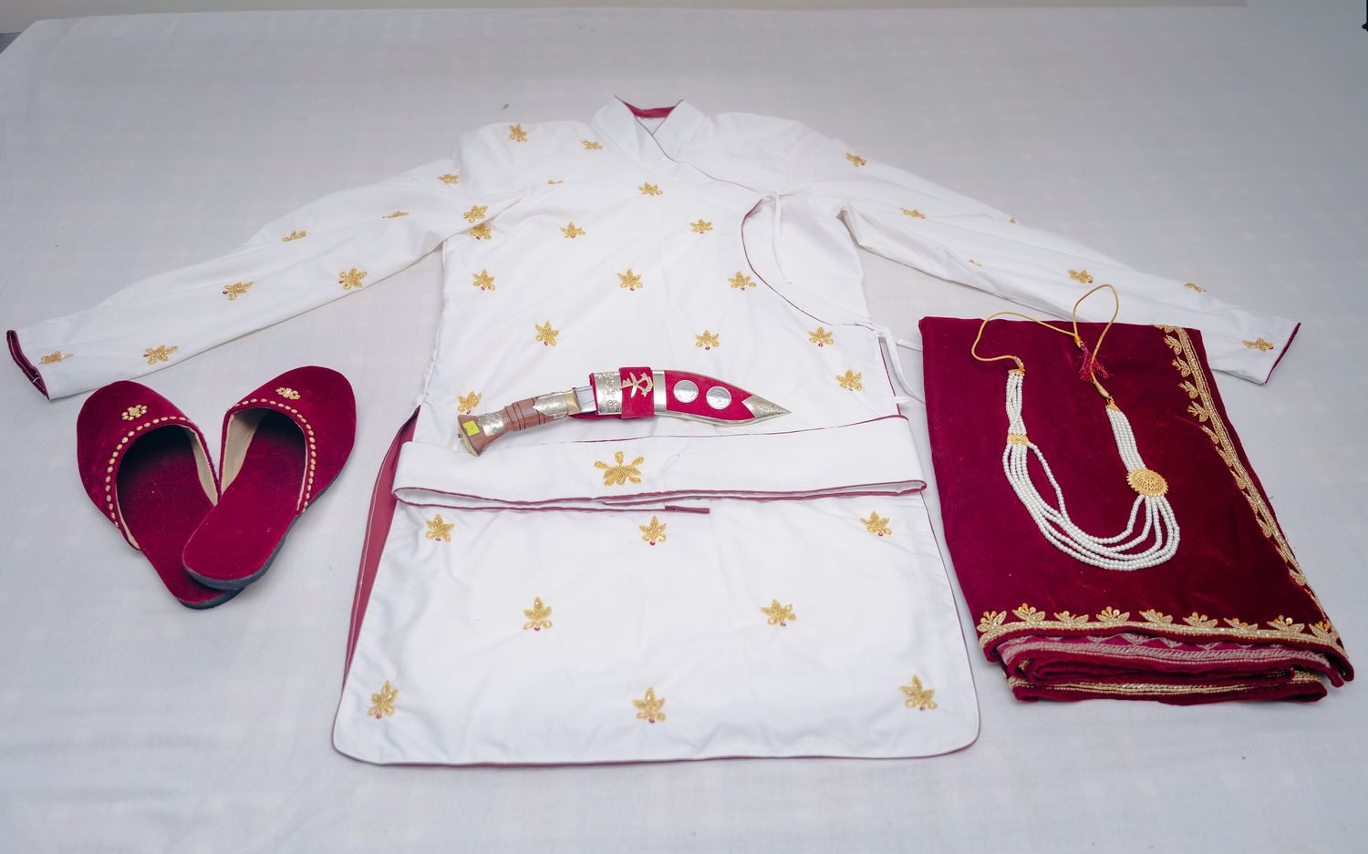 Traditional Nepali groom wedding outfit with white kurta, maroon accessories, shoes, and jewelry laid flat.