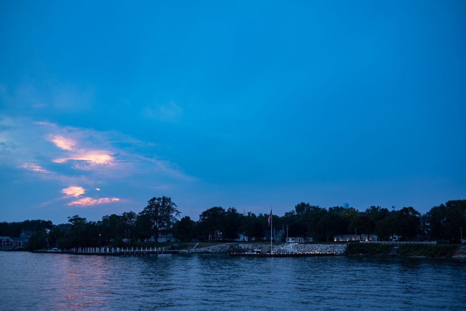 Serene dusk waterfront scene with glowing clouds reflecting on calm blue water.