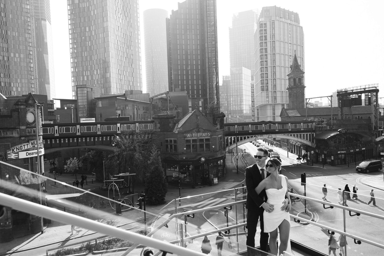 Black and white photo of a couple posing on a rooftop with a stunning city skyline backdrop.