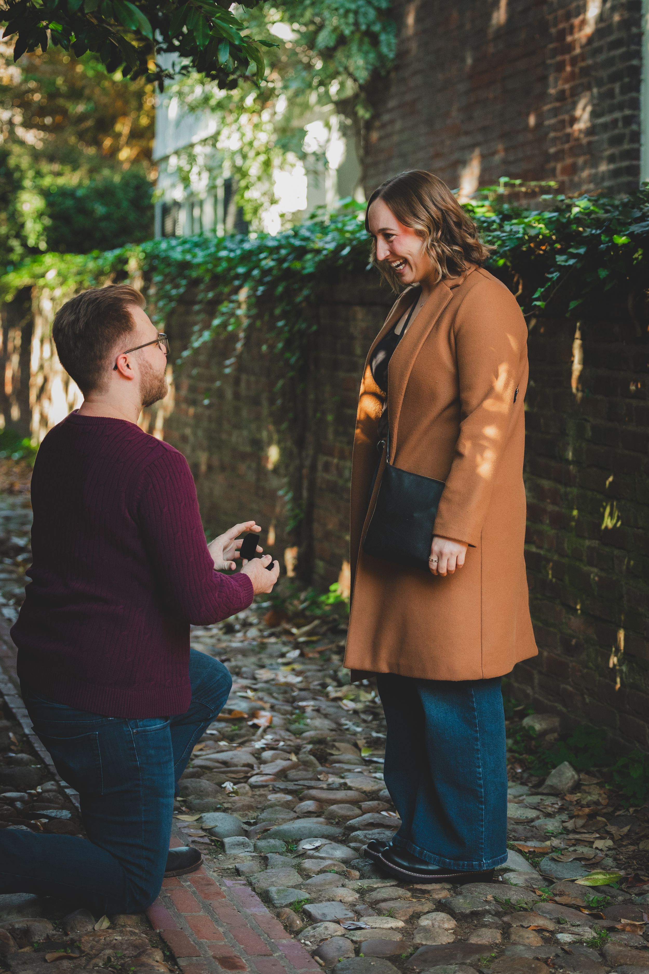 Man on one knee looking up at bride who is smiling and laughing with pure joy in a Virginia alleyway