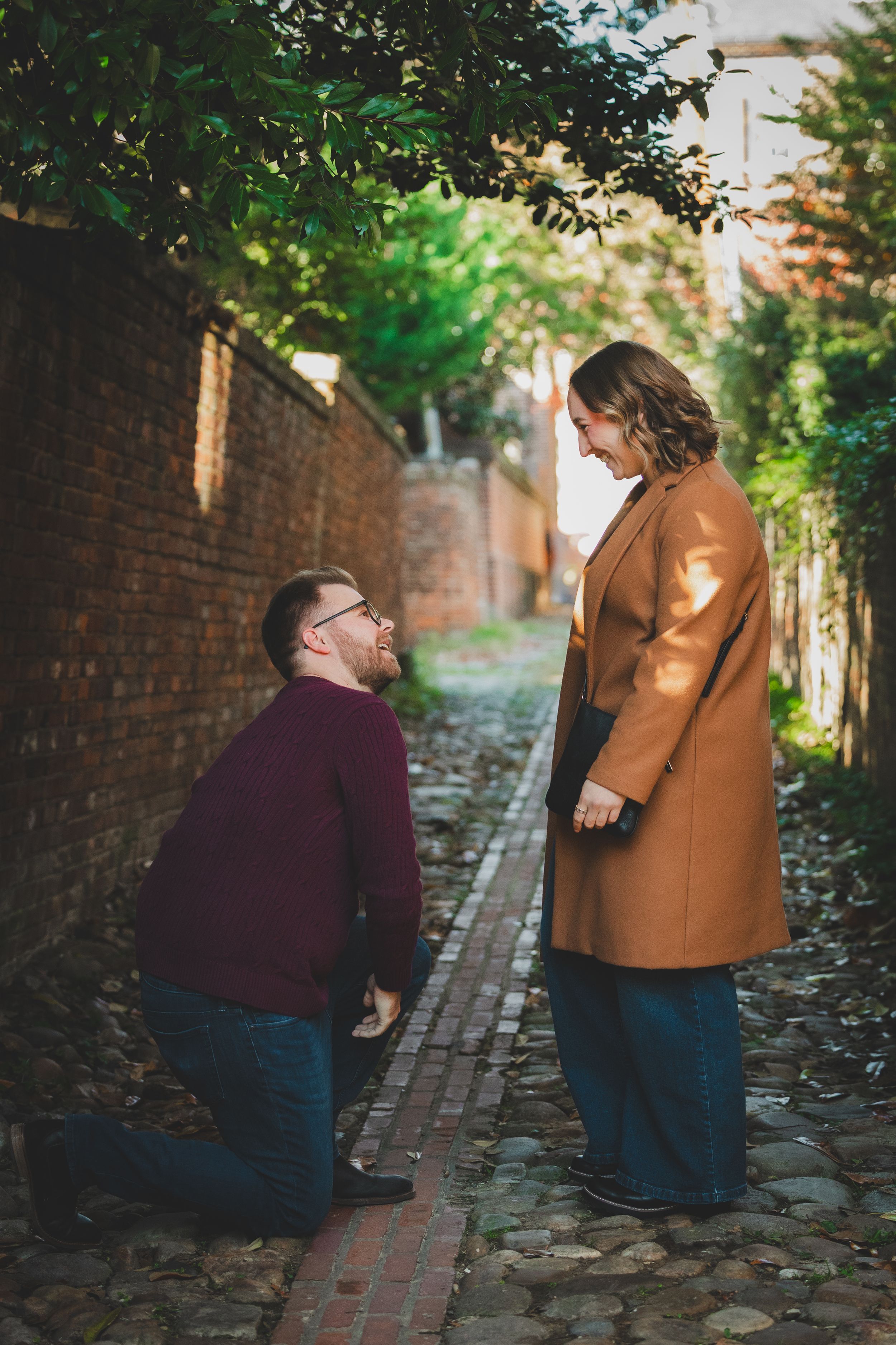 Man on one knee opening ring box as bride bursts into laughter during surprise proposal in Old Town Alexandria Virginia
