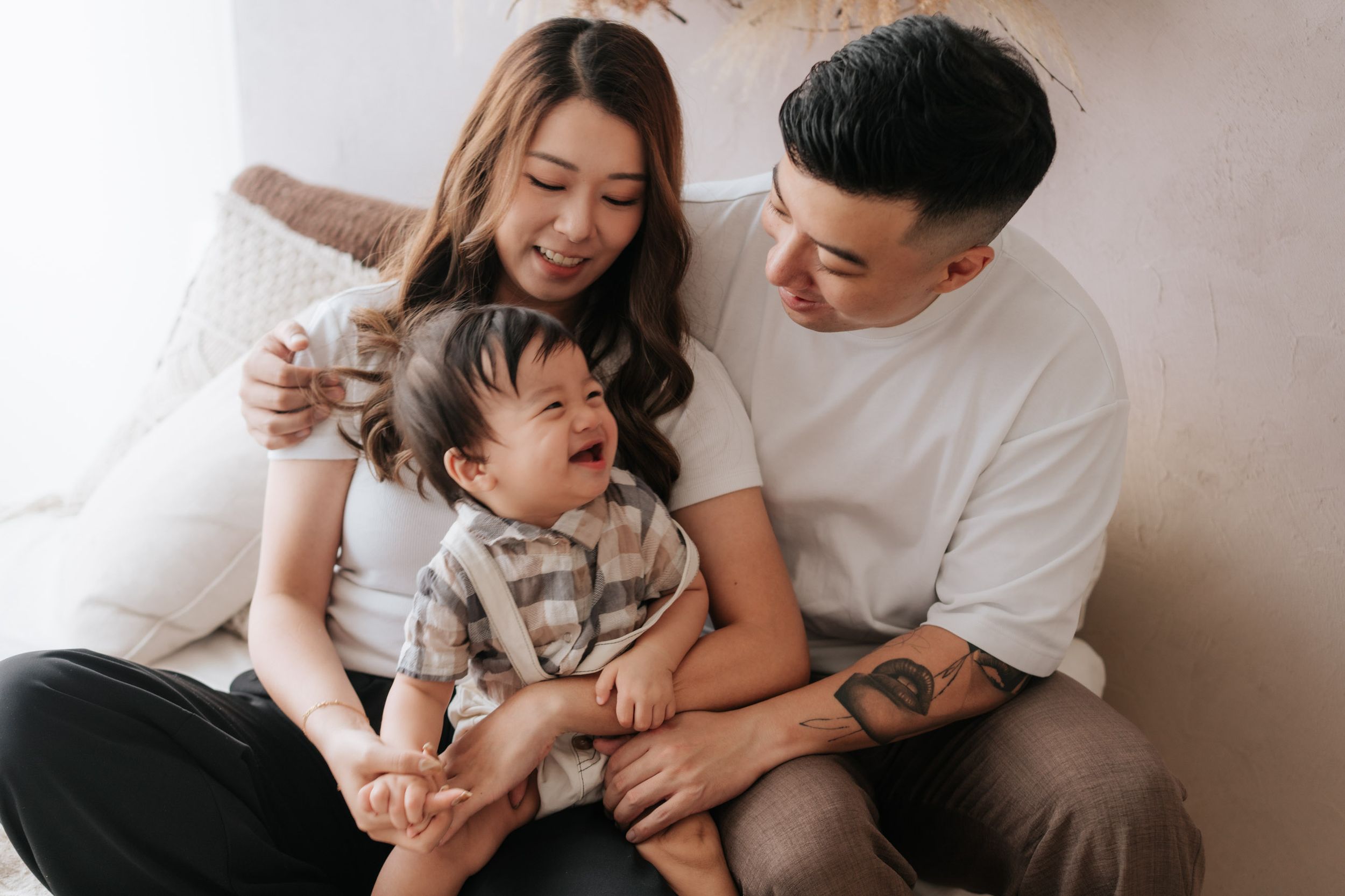 Happy Asian family with smiling parents and baby sitting together in a bright cozy room.
