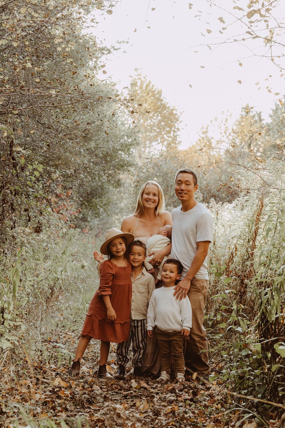 Family of six posing together on a leaf-covered forest path surrounded by autumn foliage.