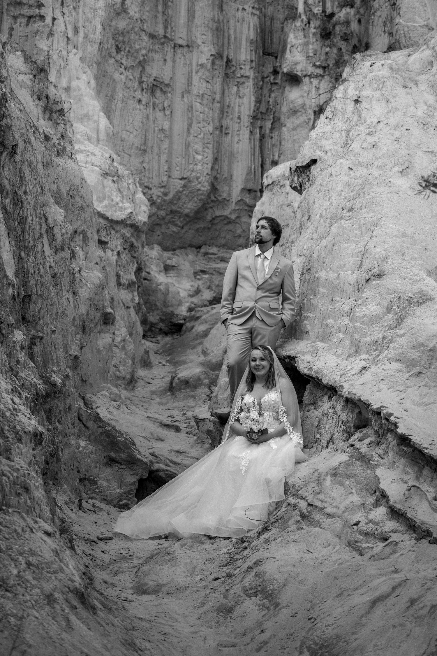 Bride and groom posing in dramatic rocky canyon landscape, black and white wedding portrait photography.