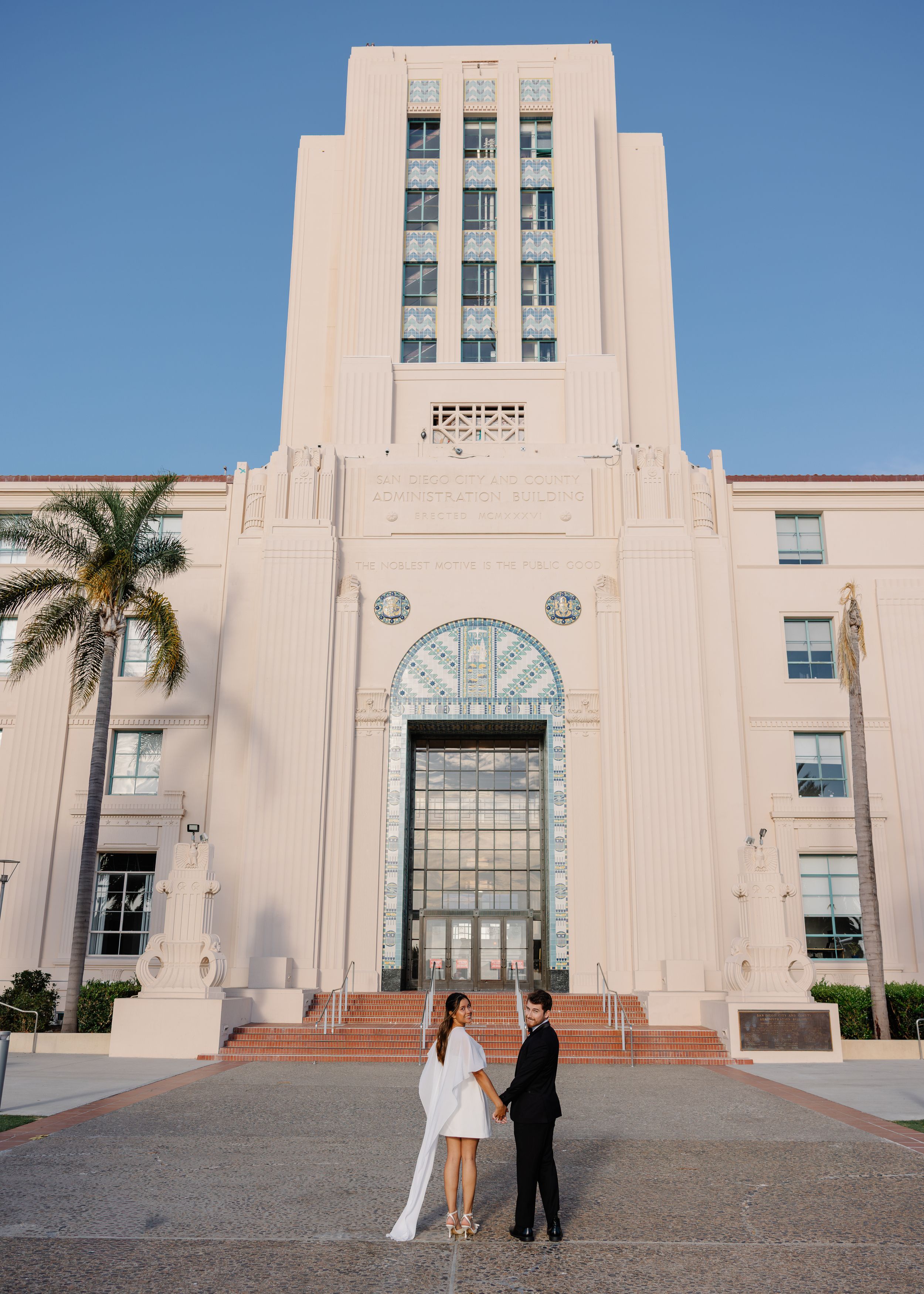 Couple holding hands in front of San Diego City Hall Art Deco building on their wedding day.