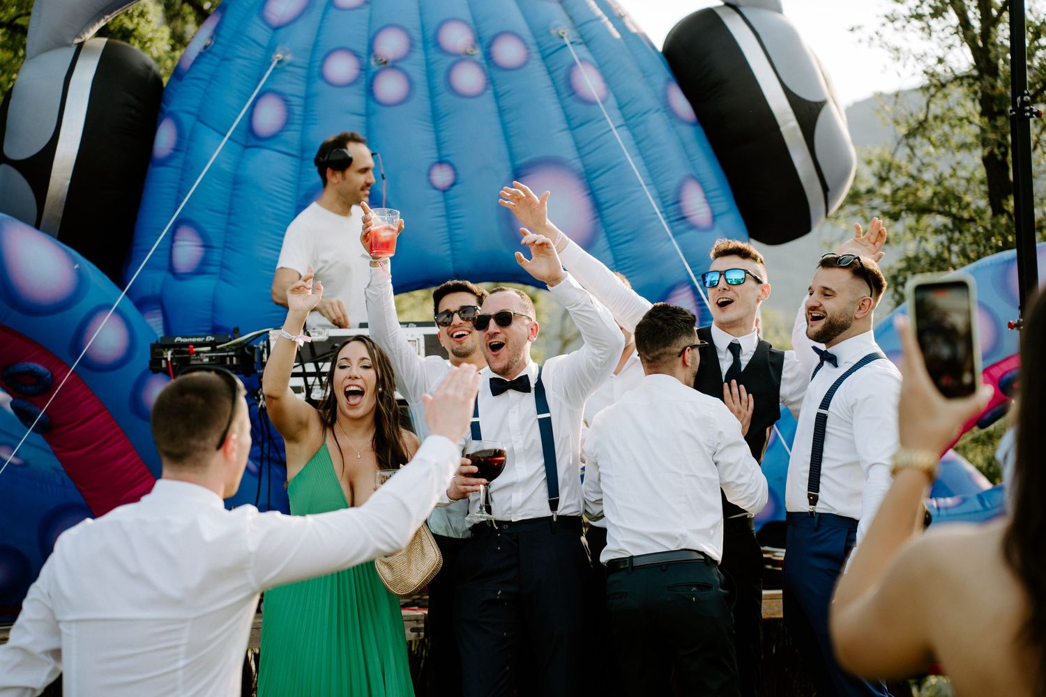 Excited wedding guests celebrating in front of large inflatable decoration at outdoor reception.