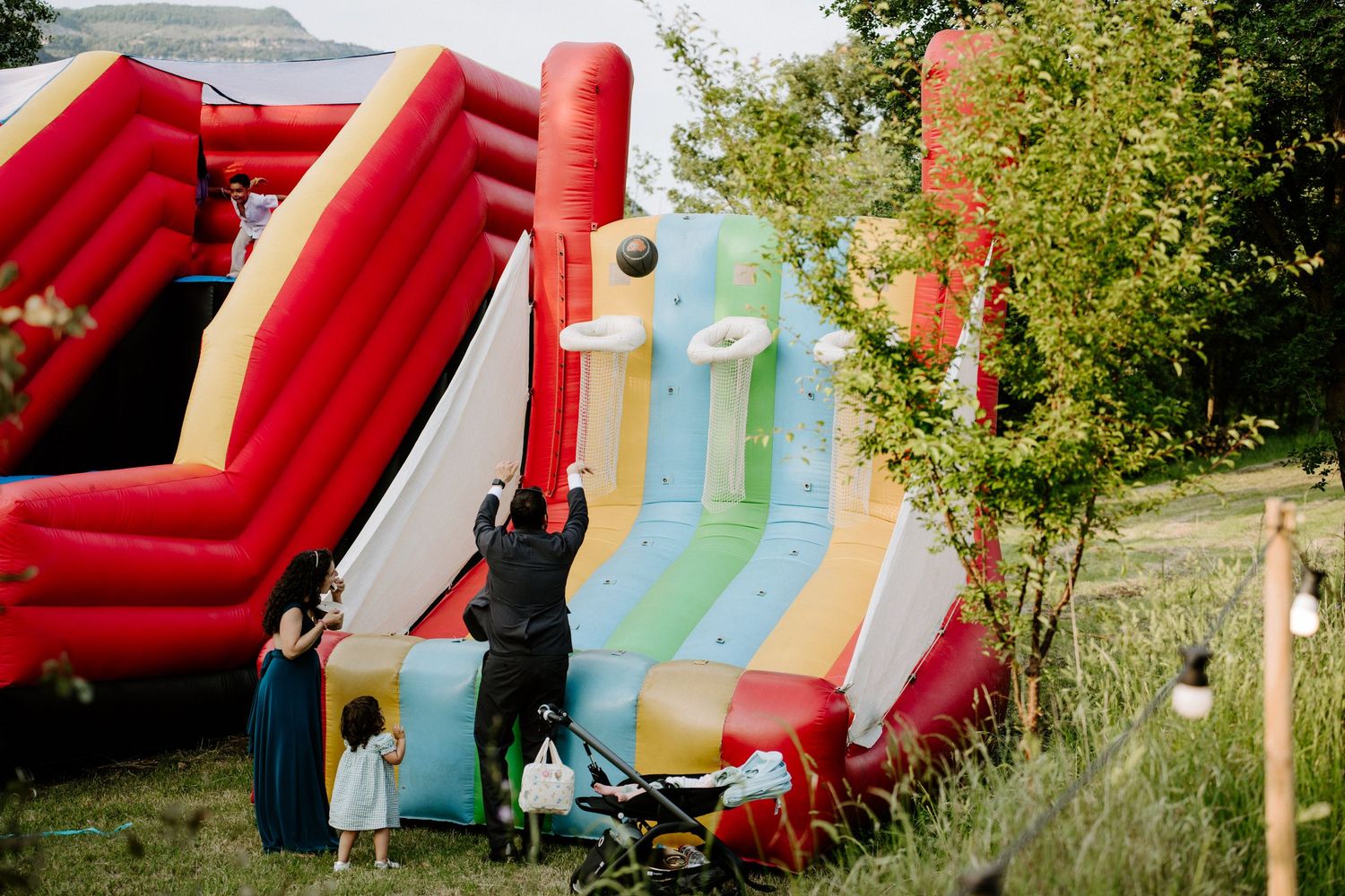 Children and adults enjoying colorful inflatable bounce house slide at outdoor wedding reception.