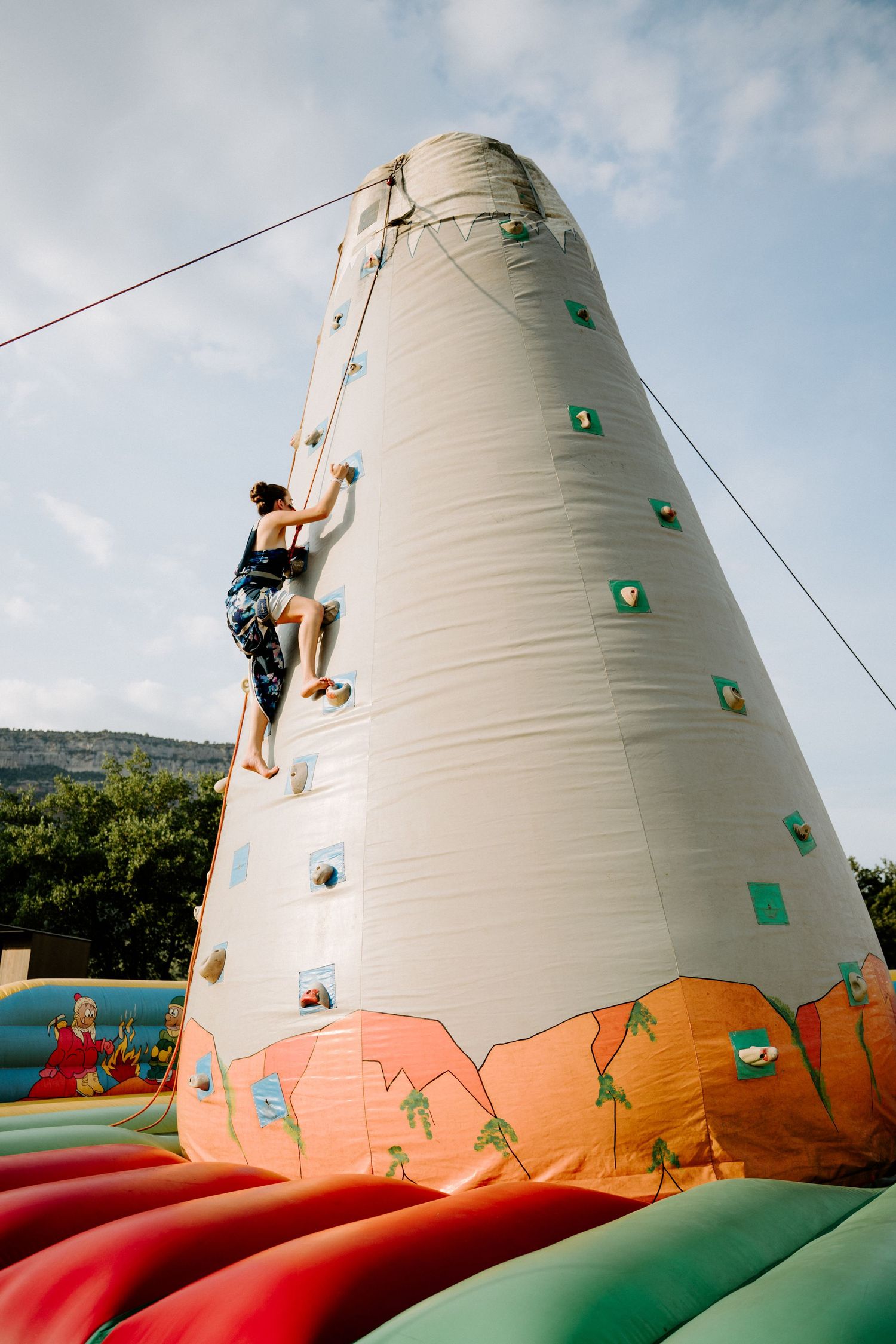 Wedding guest climbing inflatable rock climbing wall attraction at outdoor wedding reception celebration.