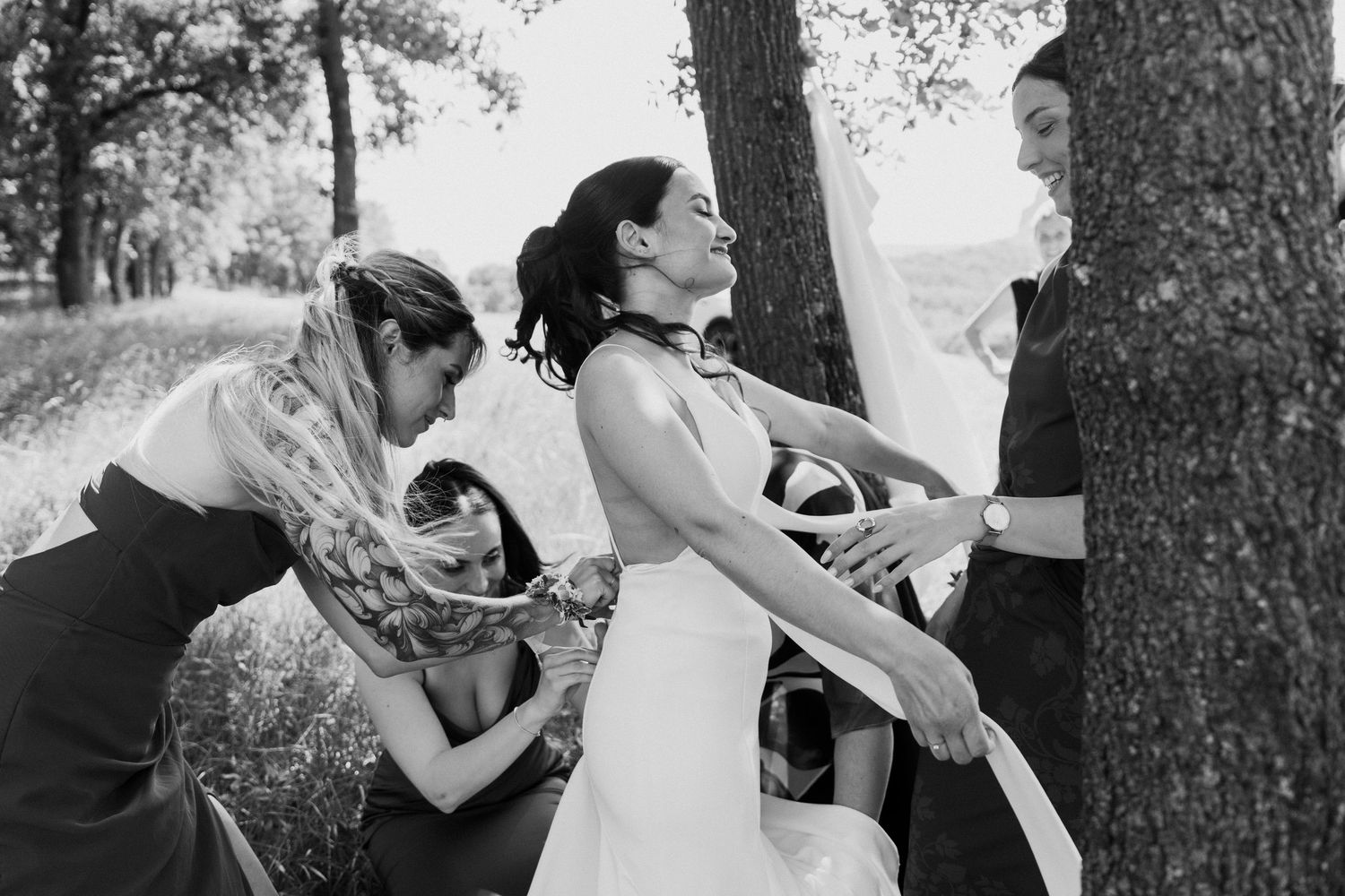 Bridesmaids helping bride adjust her wedding dress outdoors in black and white photo.