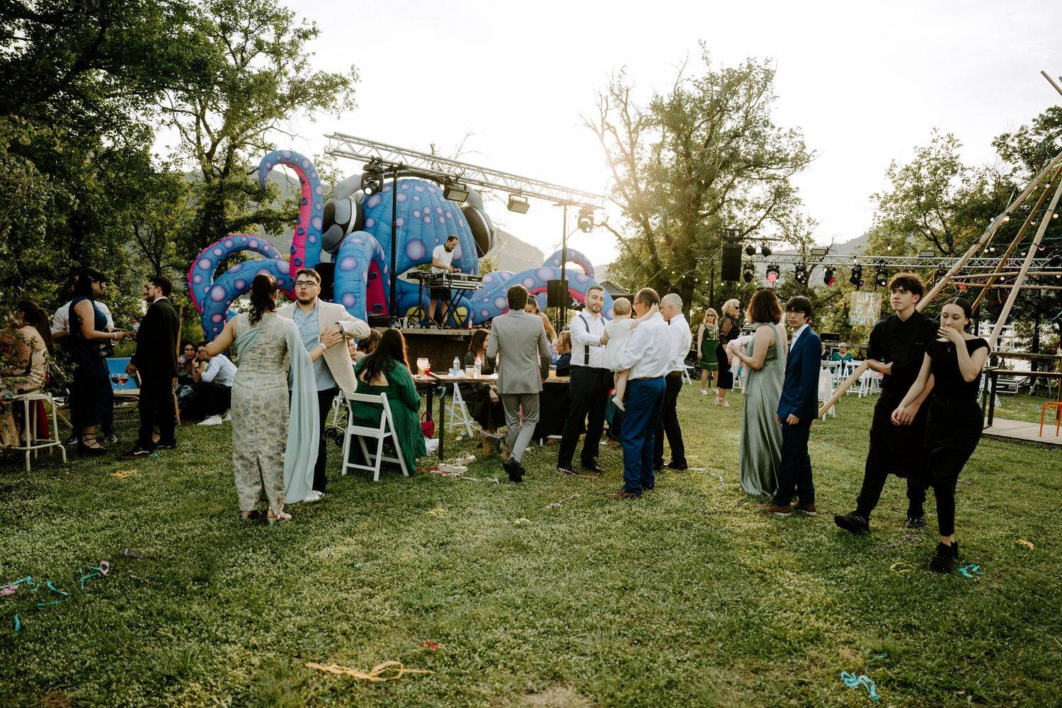 Guests mingle on a green lawn at an outdoor garden party with colorful balloon decorations and a festive backdrop.