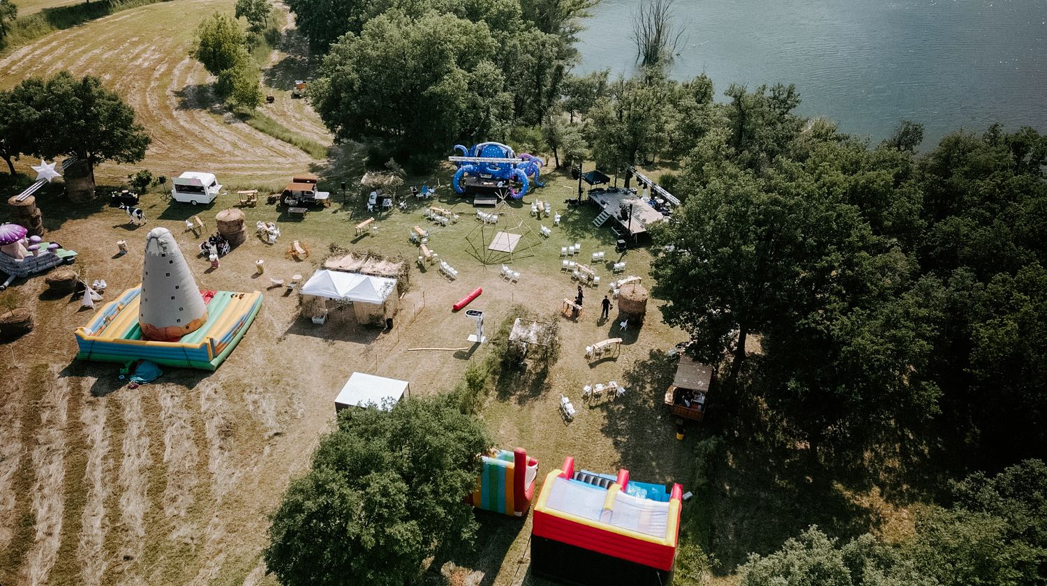 Aerial view of outdoor festival setup with inflatable attractions and tents along a riverside field.