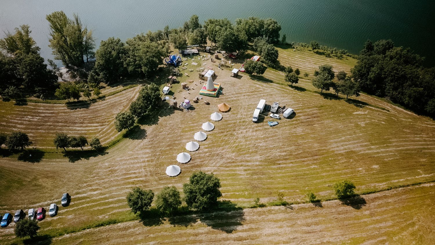 Aerial view of a riverside meadow with circular white decorations arranged in a field near water.