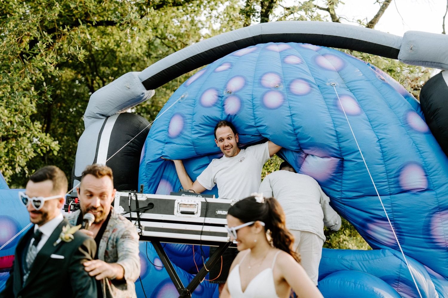 Wedding couple and guests celebrating near a colorful inflatable bounce house at an outdoor party.