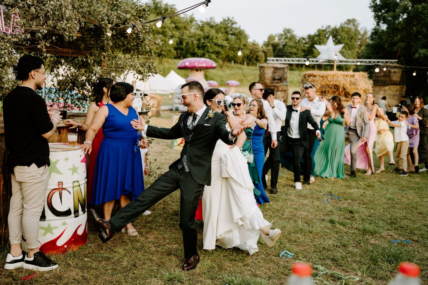 Bride and groom dancing joyfully outdoors at a colorful wedding reception with guests celebrating in the background.