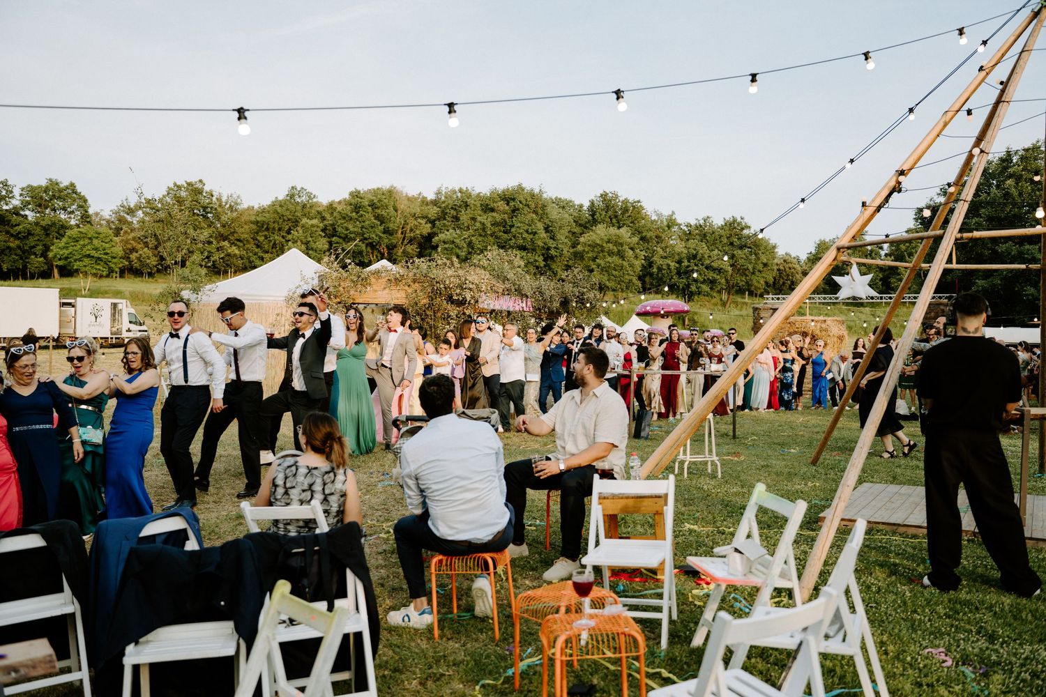 Outdoor wedding reception with guests mingling under string lights on a sunny day.