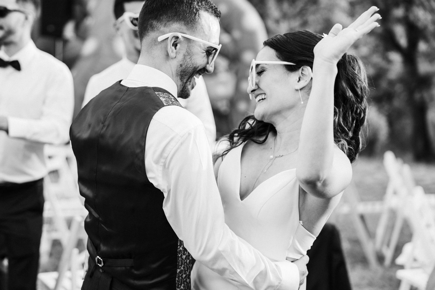 Black and white photo of a bride and groom sharing their first dance outdoors at a wedding reception.