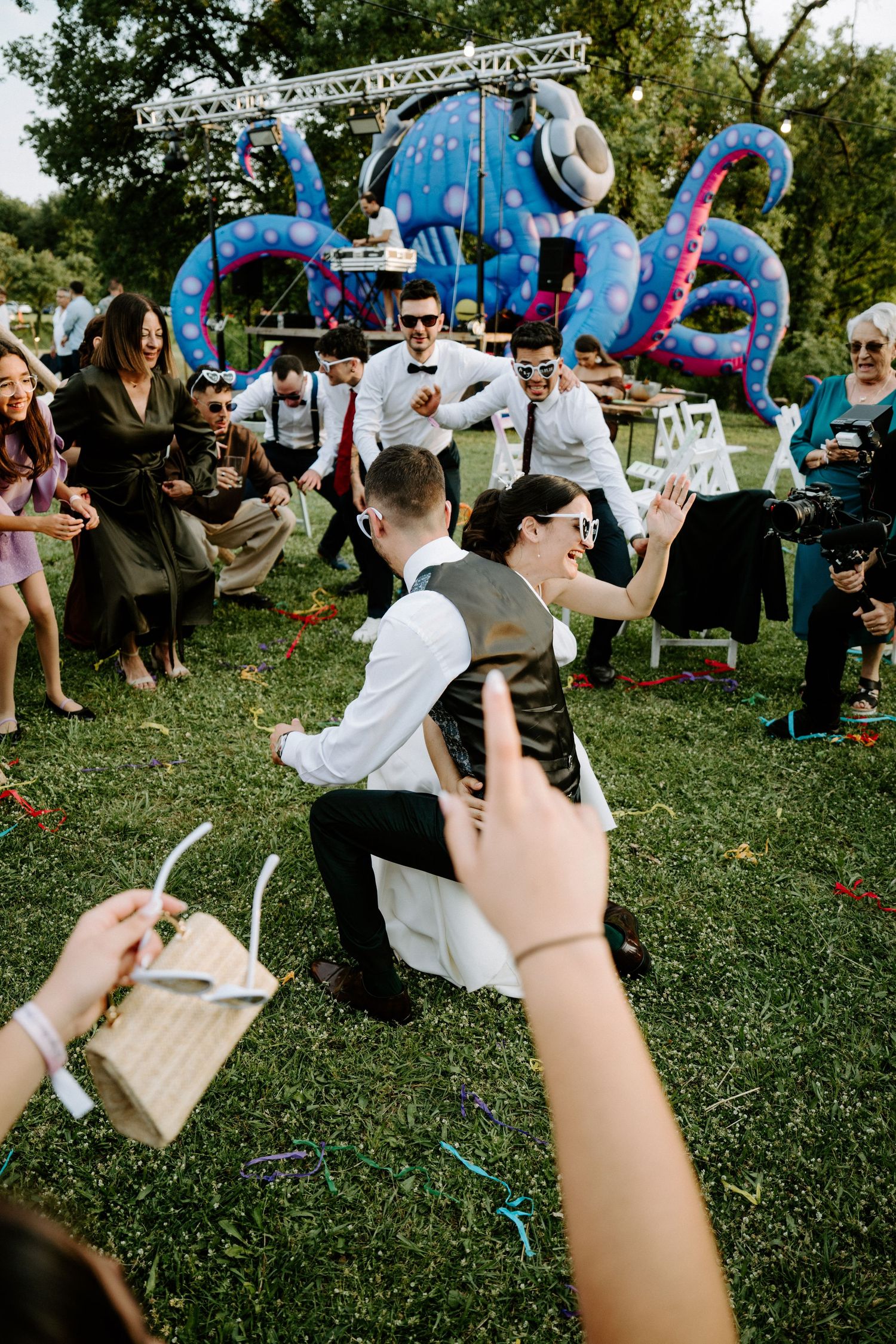 Bride and groom dancing joyfully at outdoor wedding reception with guests cheering around them.