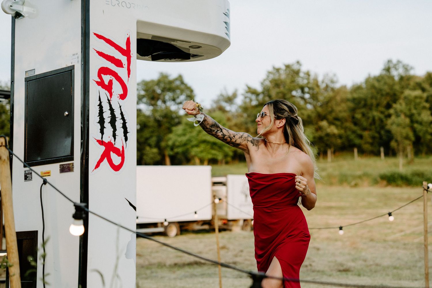 Woman in red dress posing beside a white TIGR photo booth truck at an outdoor event with string lights.