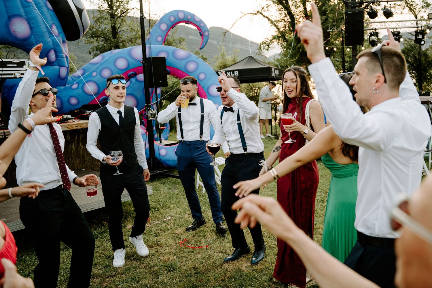 Group of young people dancing outdoors at a wedding reception near a colorful bouncy castle.
