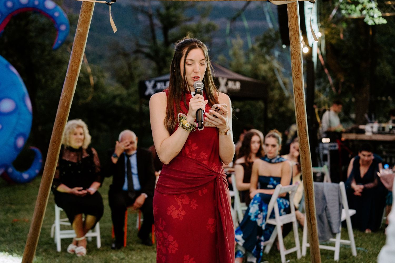 Woman in red dress reads speech at outdoor wedding ceremony.