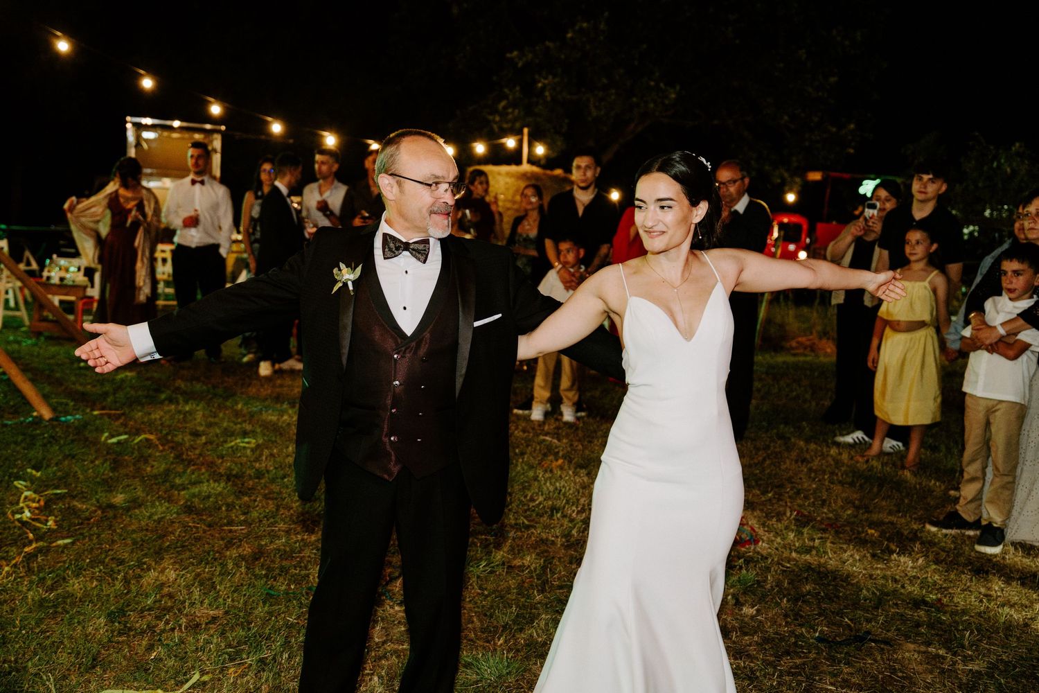 Bride in white gown and groom in black tuxedo dance together at outdoor evening wedding reception.