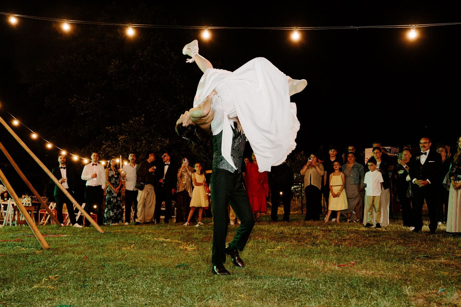 Groom lifts bride during first dance at romantic outdoor night wedding reception.