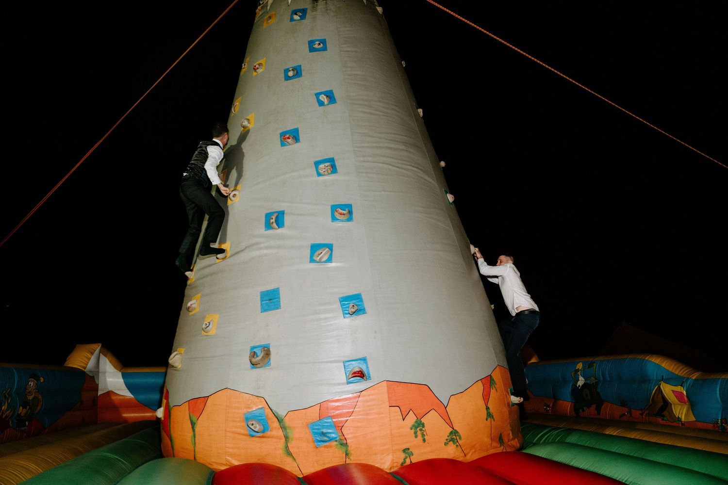 Two guests climb inflatable rock wall at fun outdoor wedding reception.