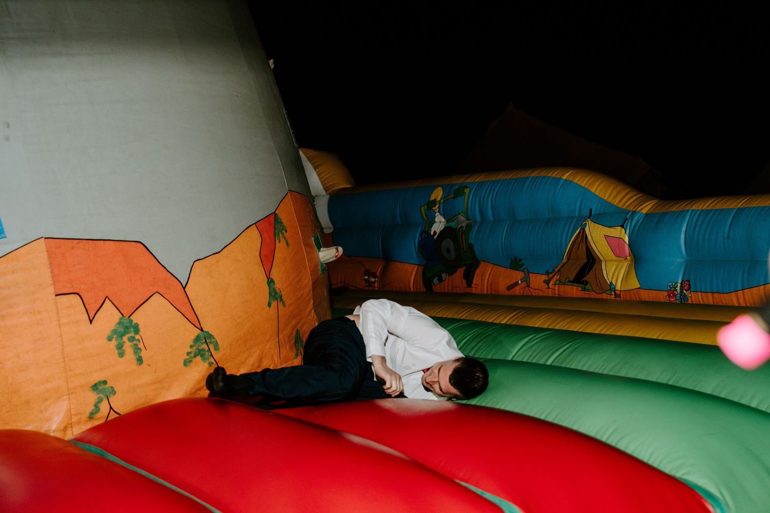Wedding guest playfully lying on a colorful inflatable bounce castle at an outdoor wedding reception.