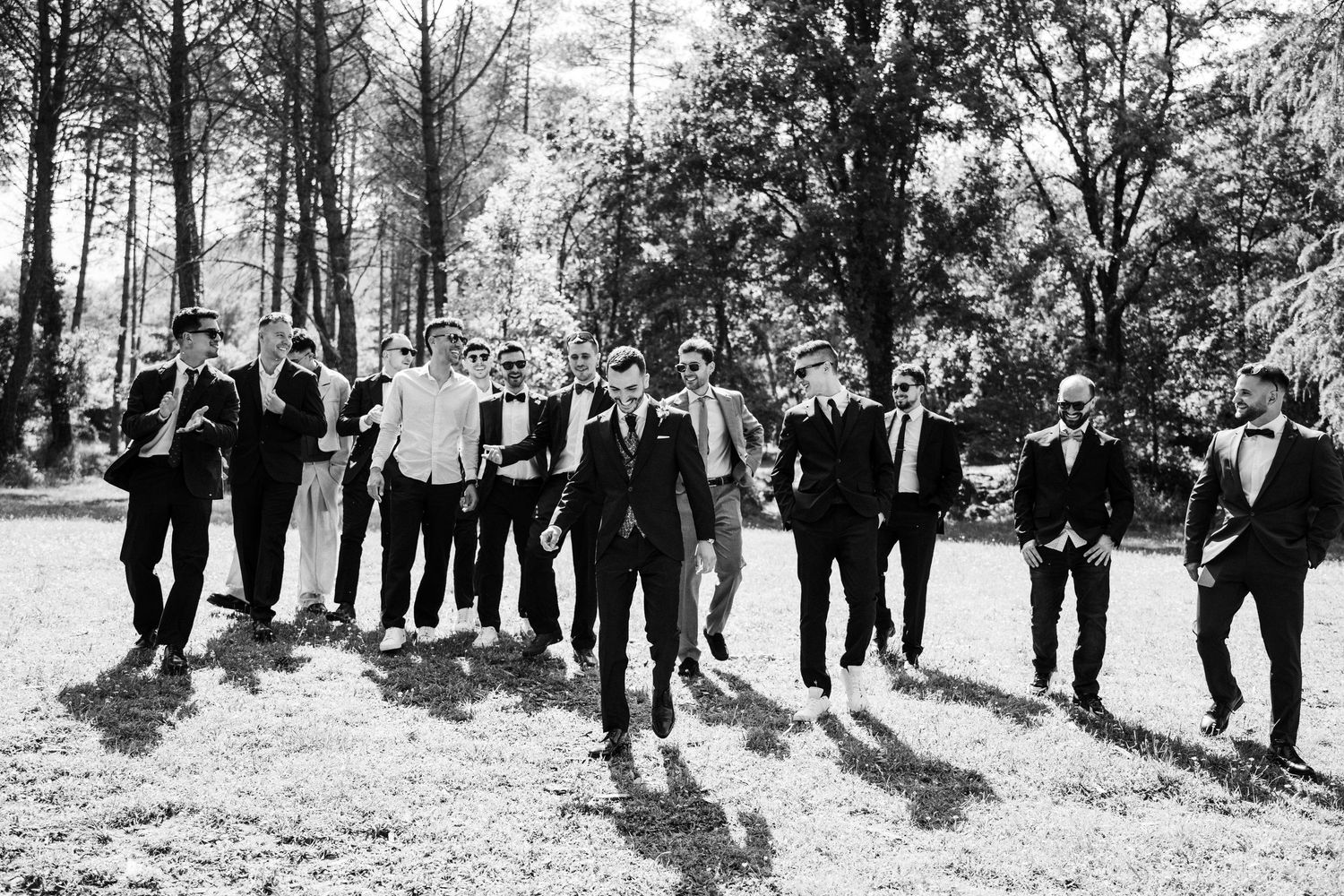 Black and white photo of groom and groomsmen walking confidently outdoors in suits.