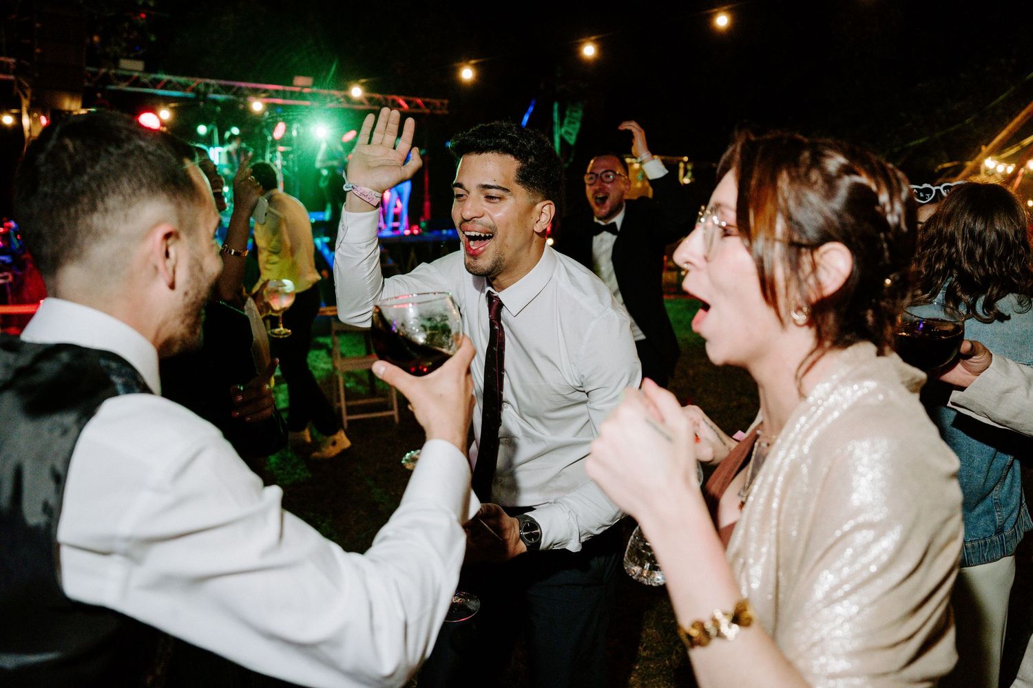 Excited wedding guests dancing and celebrating at lively outdoor reception party.
