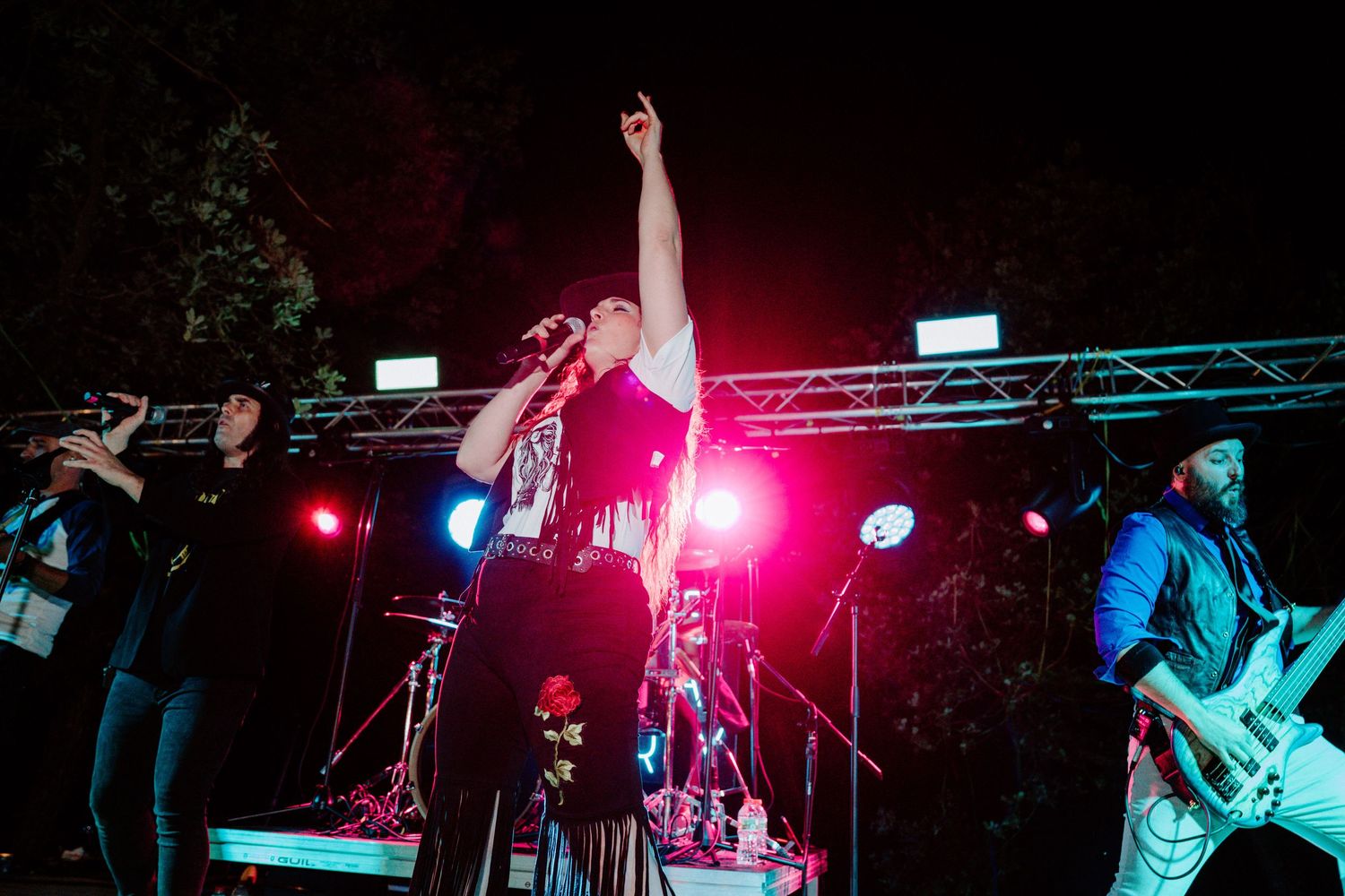 Live rock band performing on an outdoor stage at night with dramatic red and blue lighting.