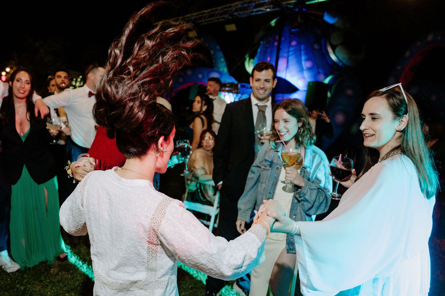 Guests dancing energetically at night wedding reception with colorful lighting and festive atmosphere.