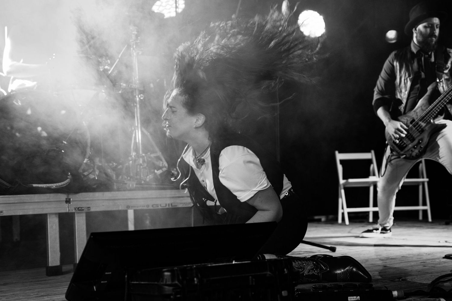 Black and white photo of a musician performing intensely on stage with a guitarist in the background.