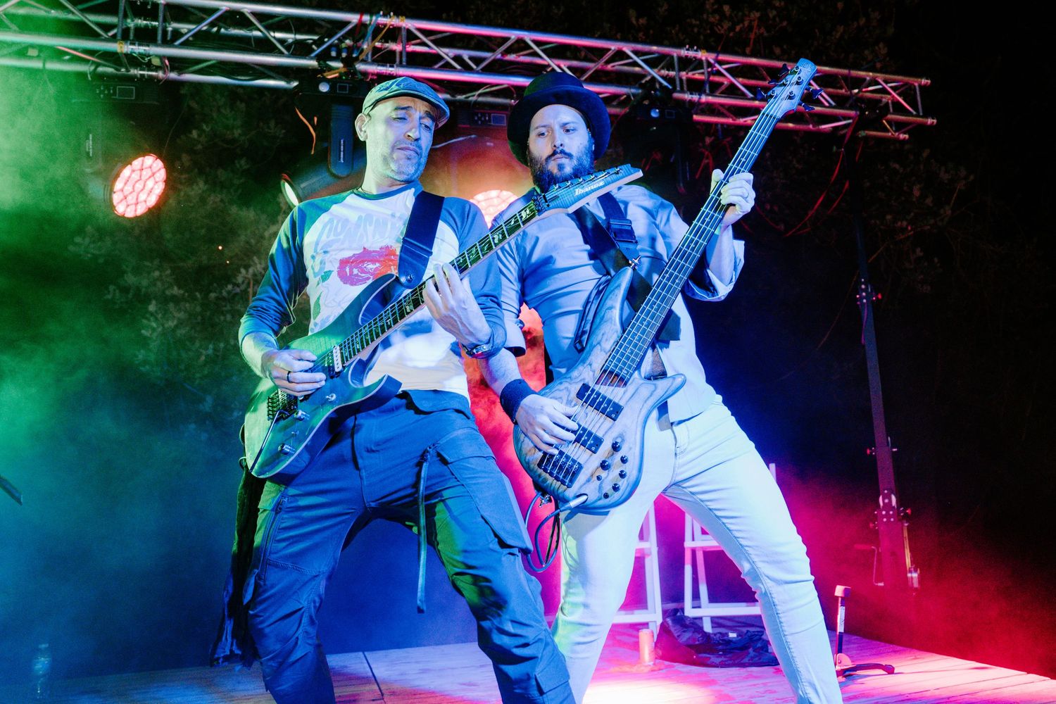 Two guitarists performing energetically on a colorful stage with green and blue lights at a live rock concert.