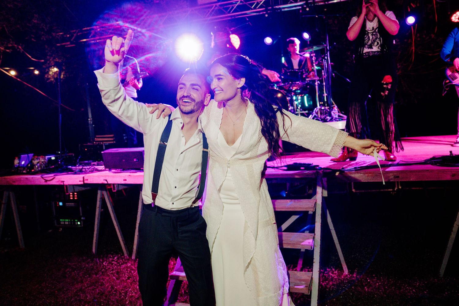 Bride and groom take a joyful selfie on the dance floor with a live band performing on stage behind them.