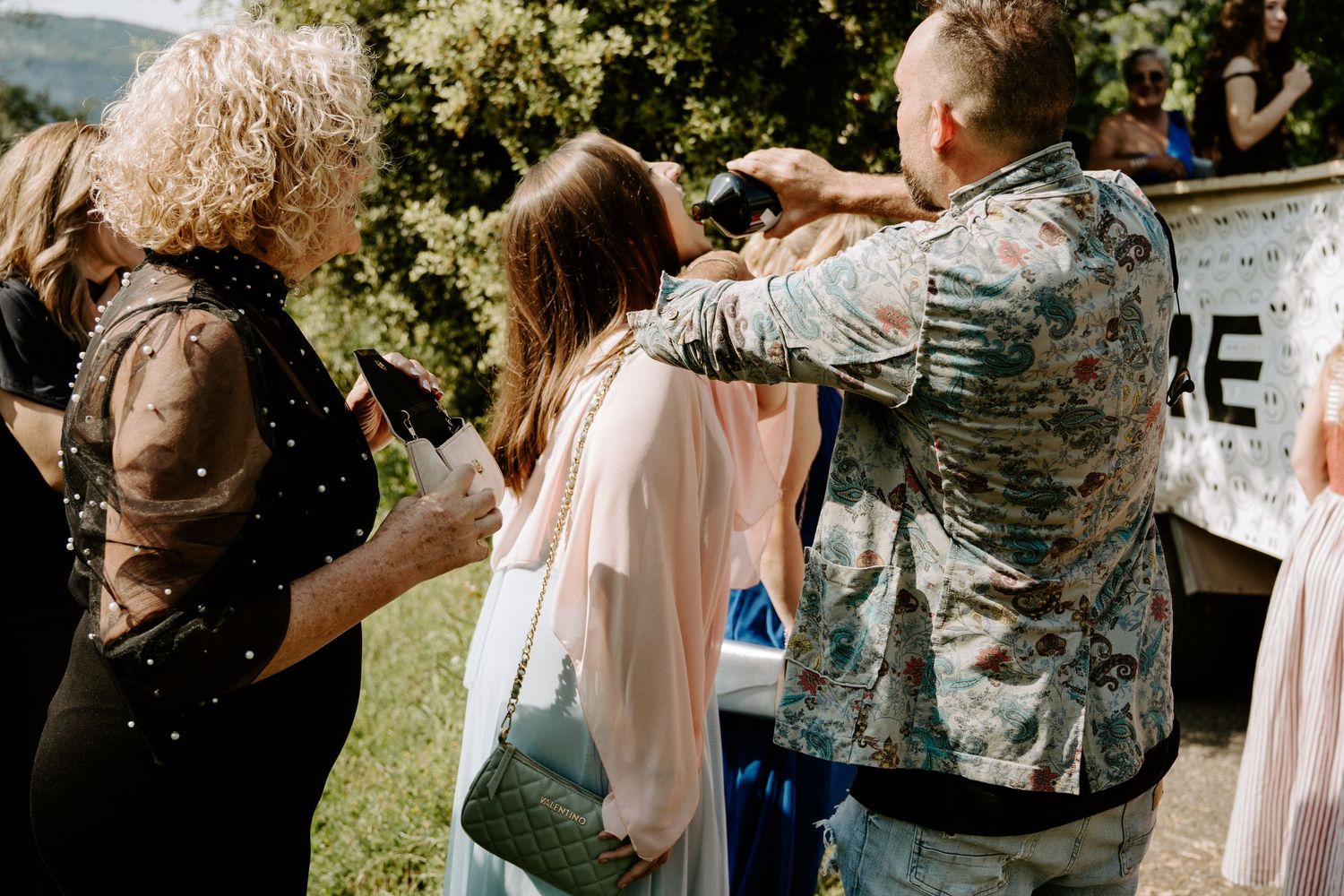 Wedding guests apply confetti to bride's hair during outdoor celebration at scenic venue.