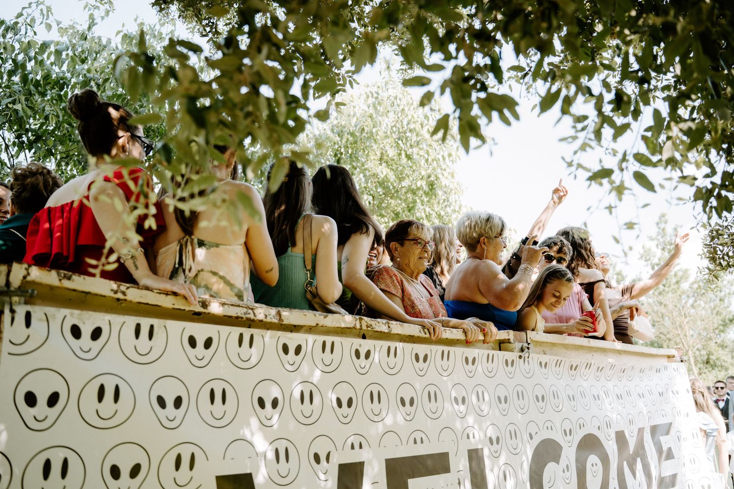 Group of festive people gathered on decorated float with welcome sign at outdoor event.