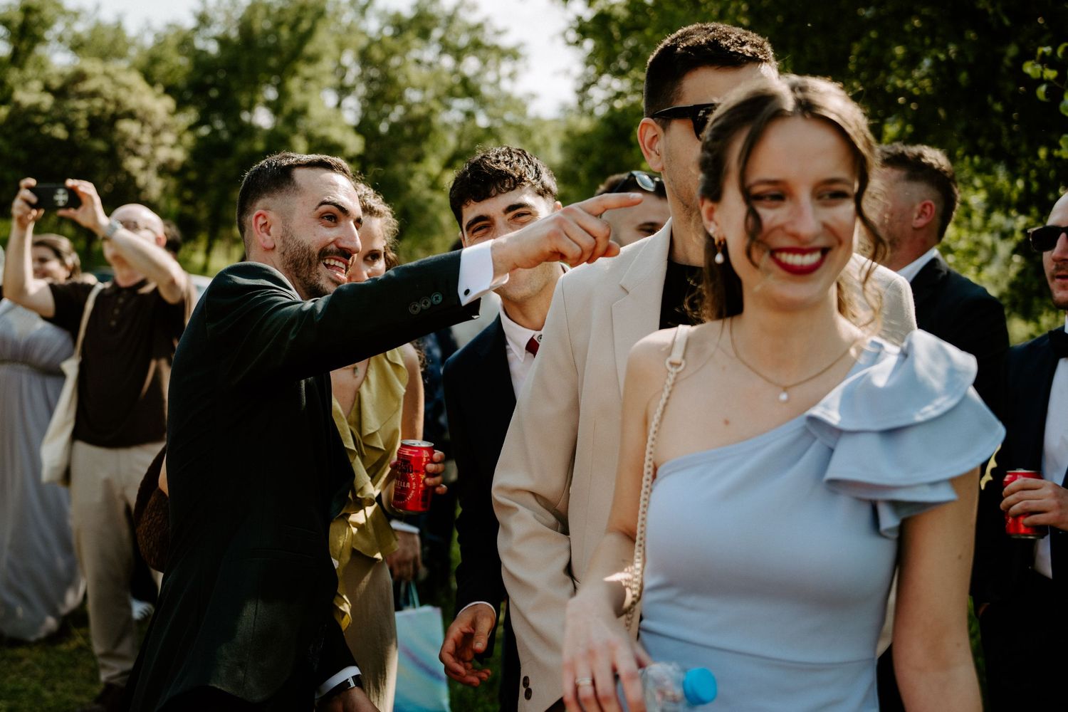 Wedding guests laugh and celebrate outdoors on a sunny day during a festive reception.