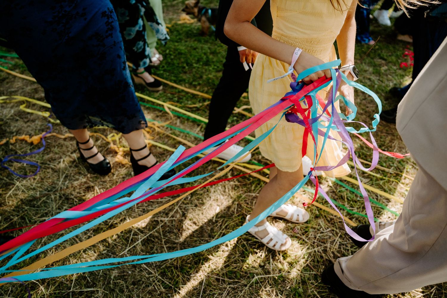 Colorful ribbons held by wedding guests during a maypole dance activity on straw-covered ground.