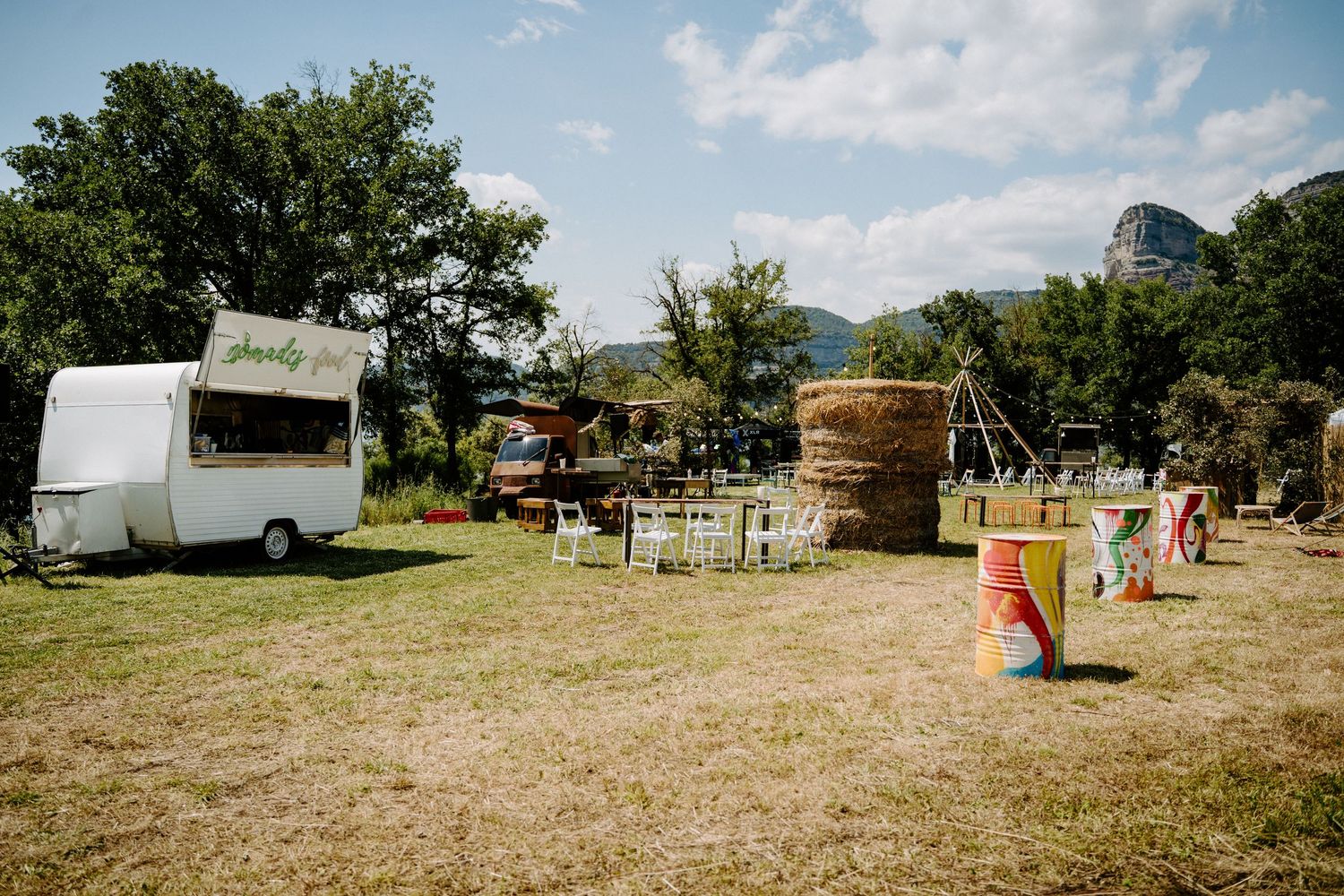 Rustic outdoor wedding venue with a vintage white food trailer, hay bales, and colorful decorations on a sunny day.