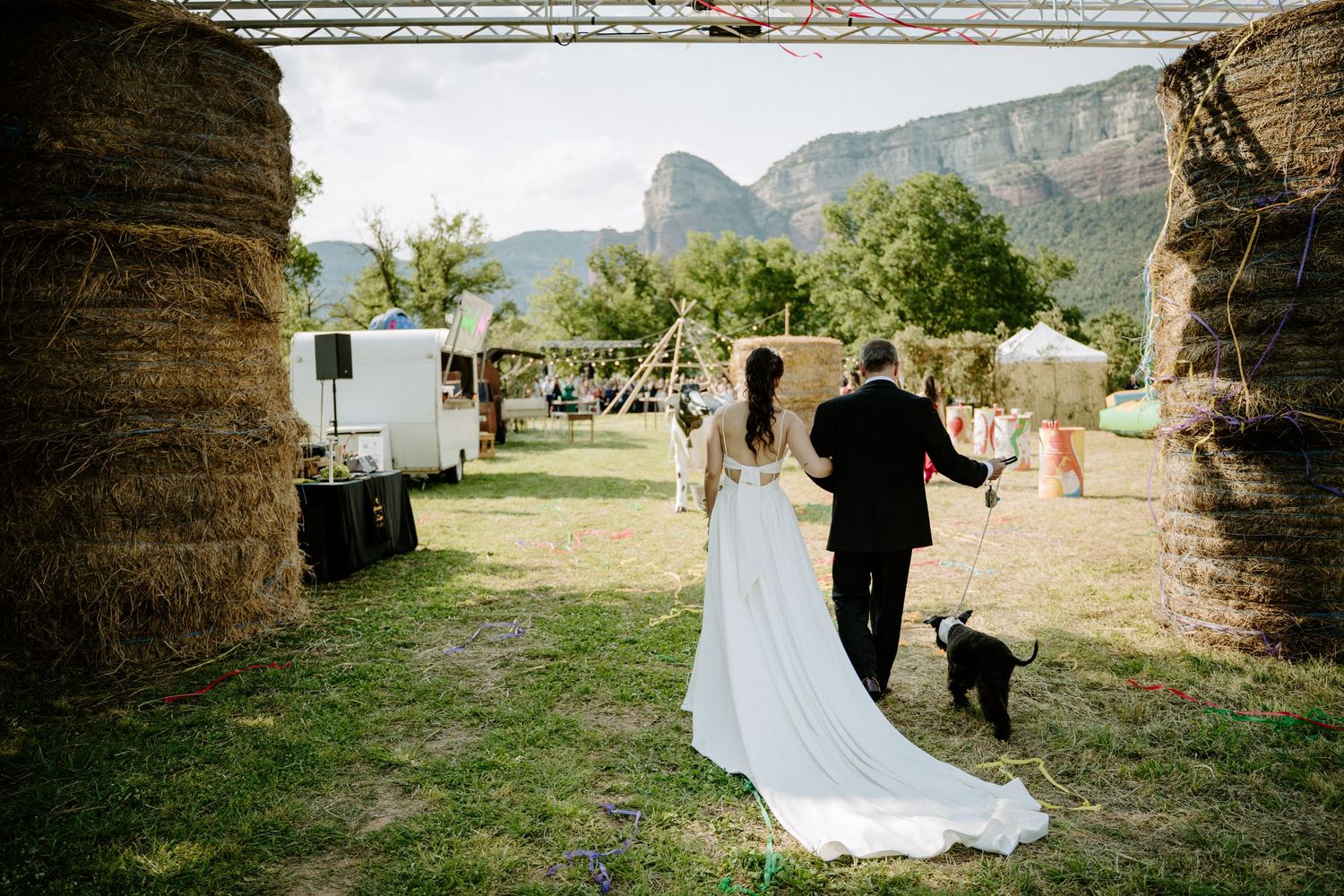 Bride and groom walking hand in hand through rustic farm wedding venue with mountain backdrop.