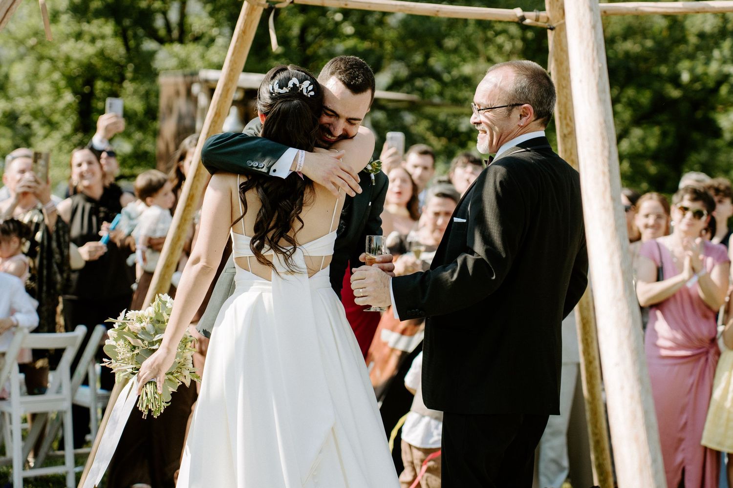 Bride and groom sharing first kiss under wooden arch at outdoor garden wedding ceremony.