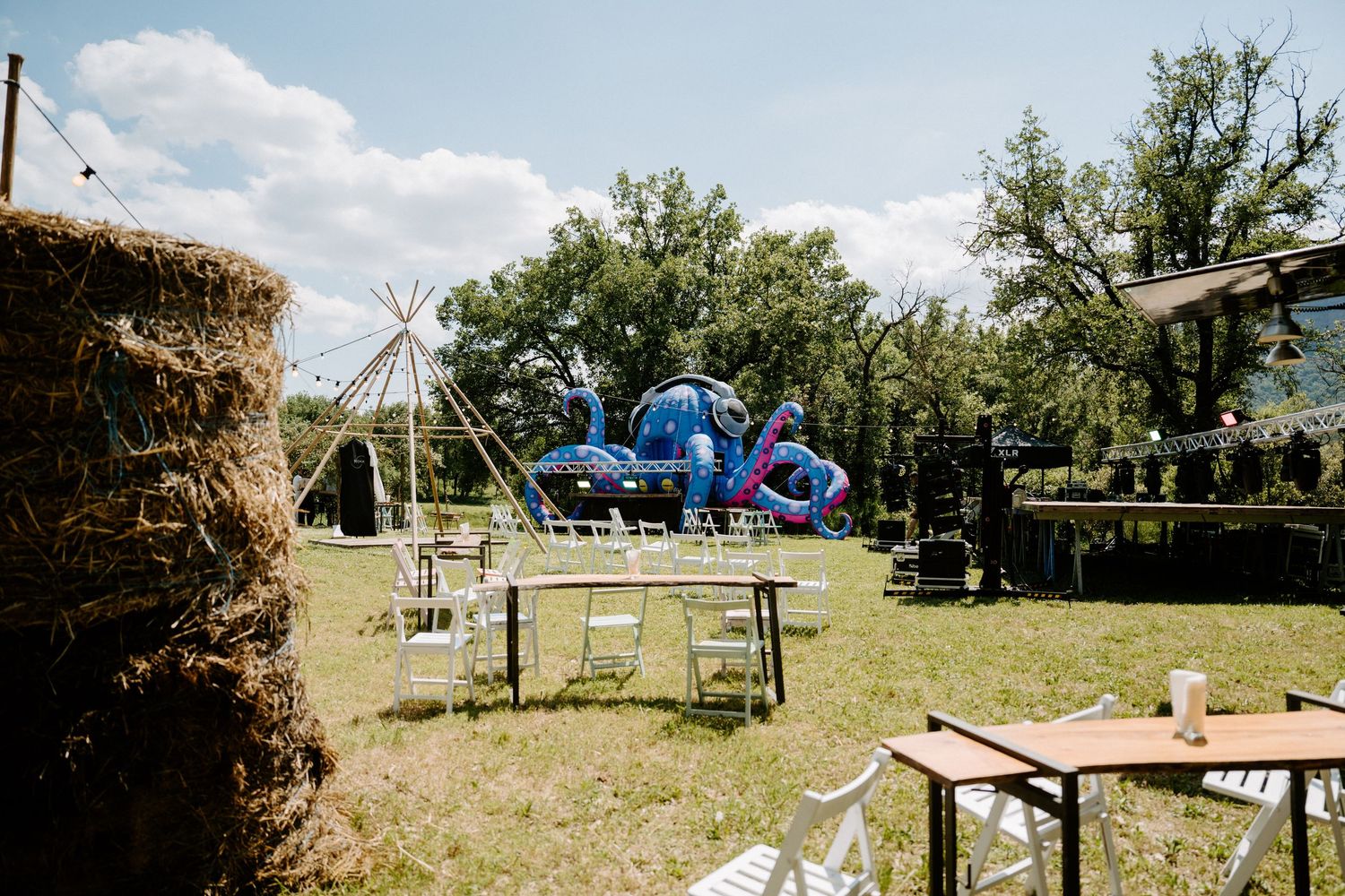 Rustic outdoor wedding venue with hay bales, white chairs, and colorful inflatable octopus decoration.