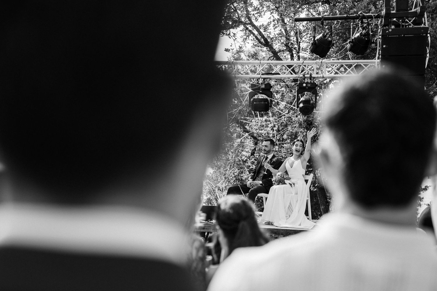Black and white photo of wedding ceremony outdoors with officiant speaking to seated guests.