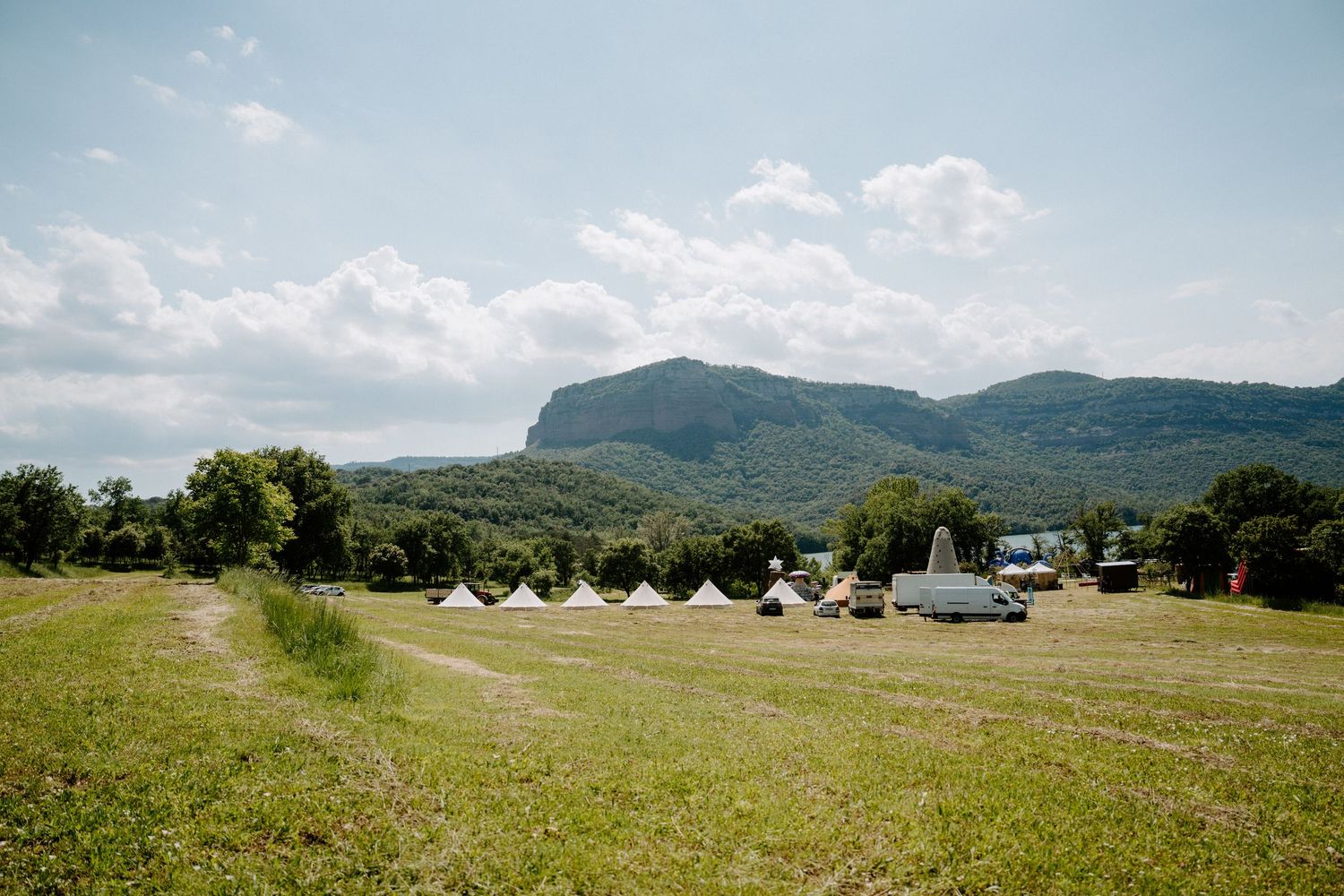 Scenic outdoor wedding venue with white bell tents in a green field beneath a dramatic mountain backdrop.