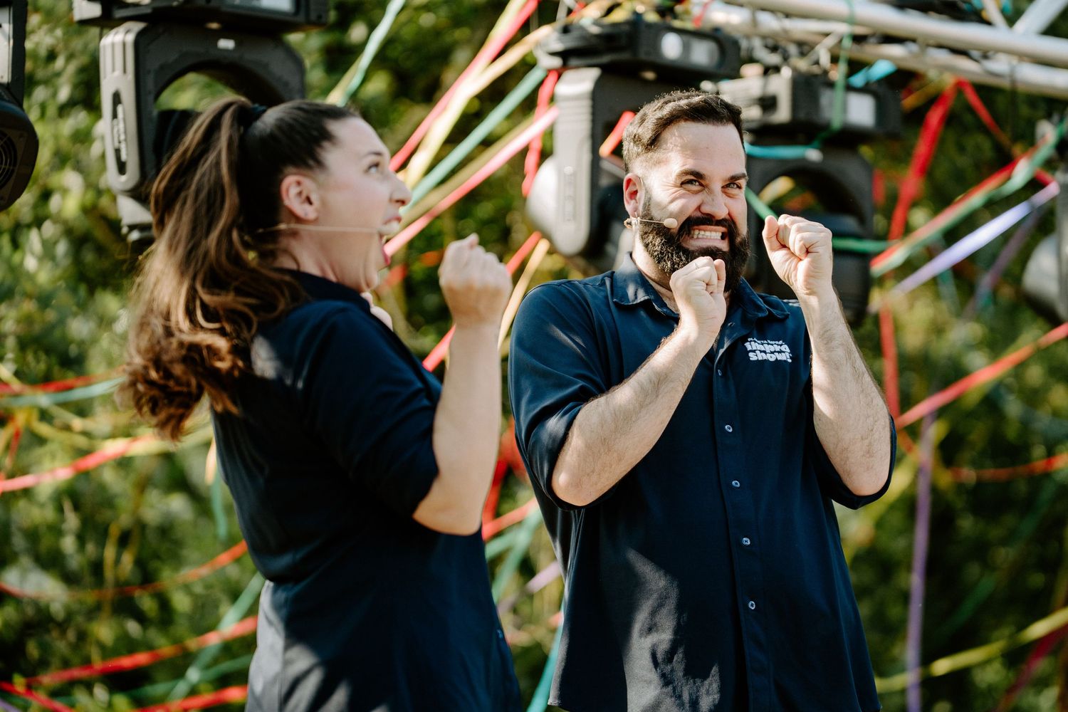 Two wedding staff members in navy shirts celebrating joyfully with fist pumps at outdoor event.