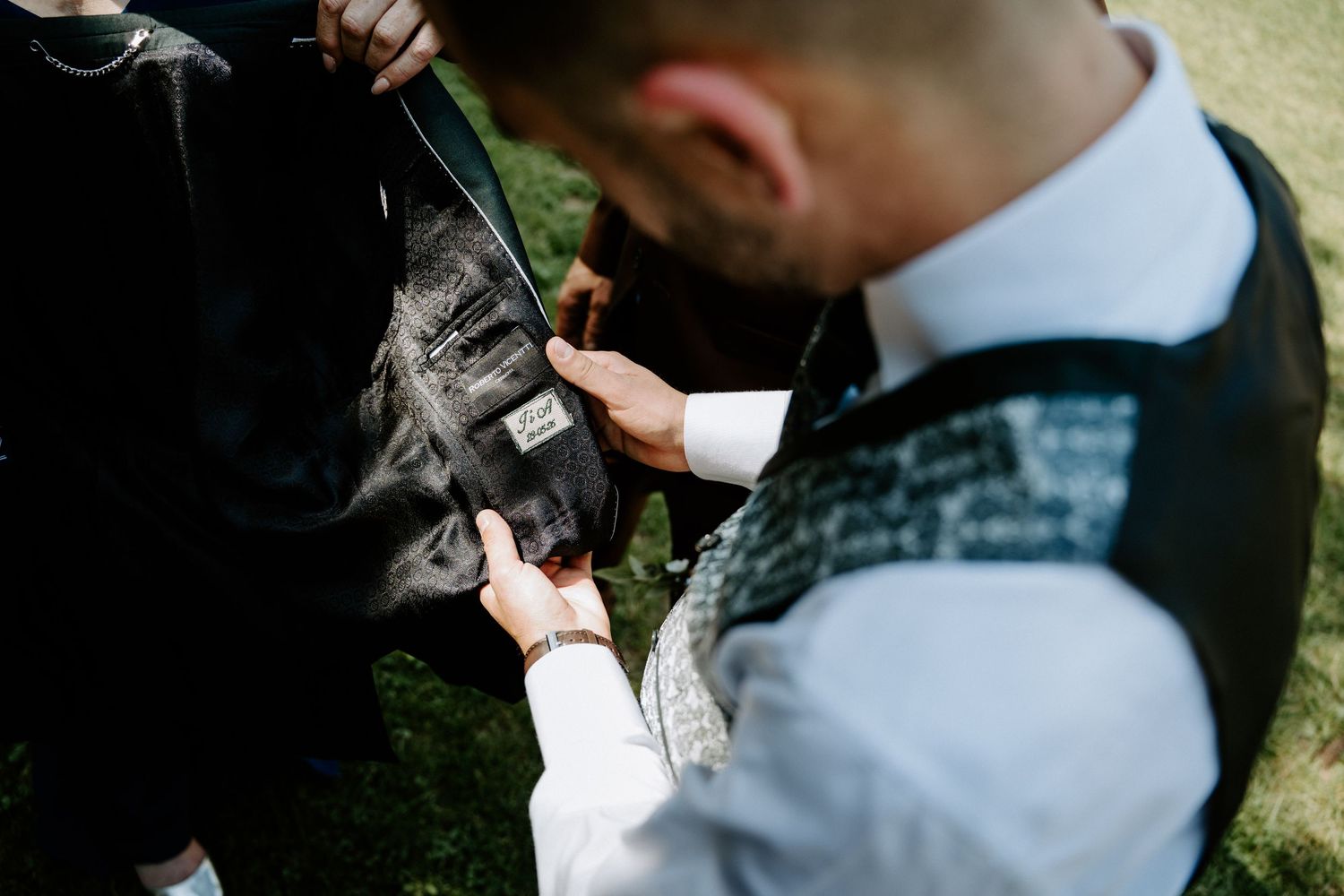 Groom adjusting suit jacket label outdoors on wedding day.