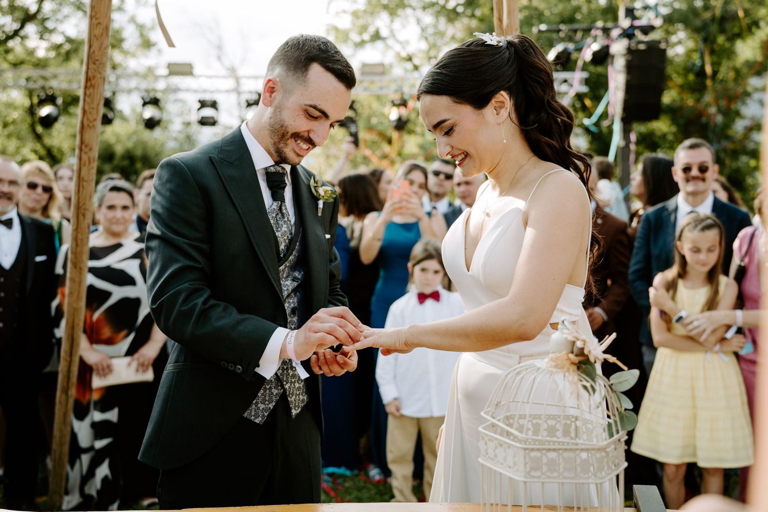 Smiling bride and groom exchanging rings during an outdoor wedding ceremony.