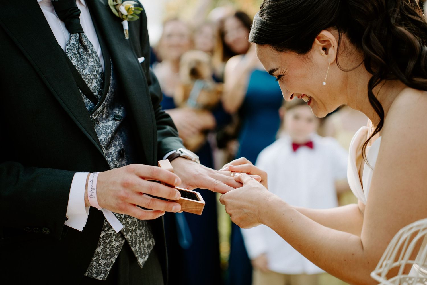 Close-up of bride placing wedding ring on grooms finger during outdoor ceremony.