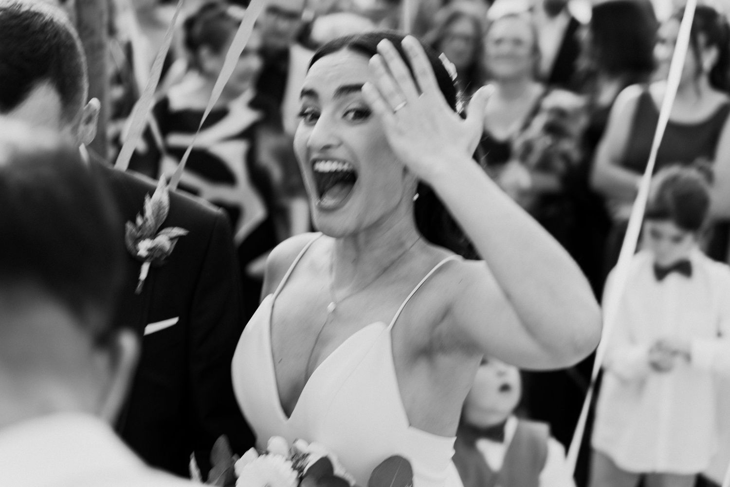 Black and white photo of overjoyed bride showing off wedding ring to cheering guests.